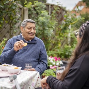 This is an image of two people talking to each other, with one eating a biscuit and the other having a drink.