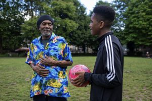 This is an image of an older man and a younger man, who is holding a ball, in a park.