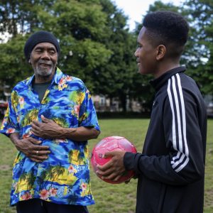 This is an image of an older man and a younger man, who is holding a ball, in a park.