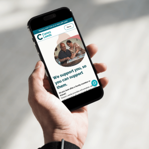 This is an image of a person holding a phone looking at the Carers Leeds website.