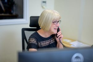This is an image of woman behind a computer, on the phone smiling.