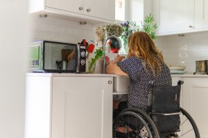 Image of a woman in a wheelchair in a kitchen, at an adapted sink.