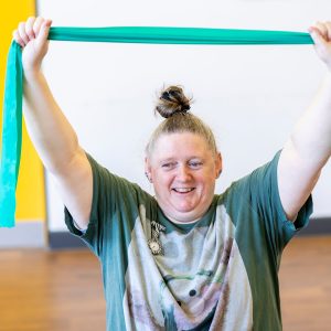 Image of a woman exercising. Her arms are above her head holding an exercise towel